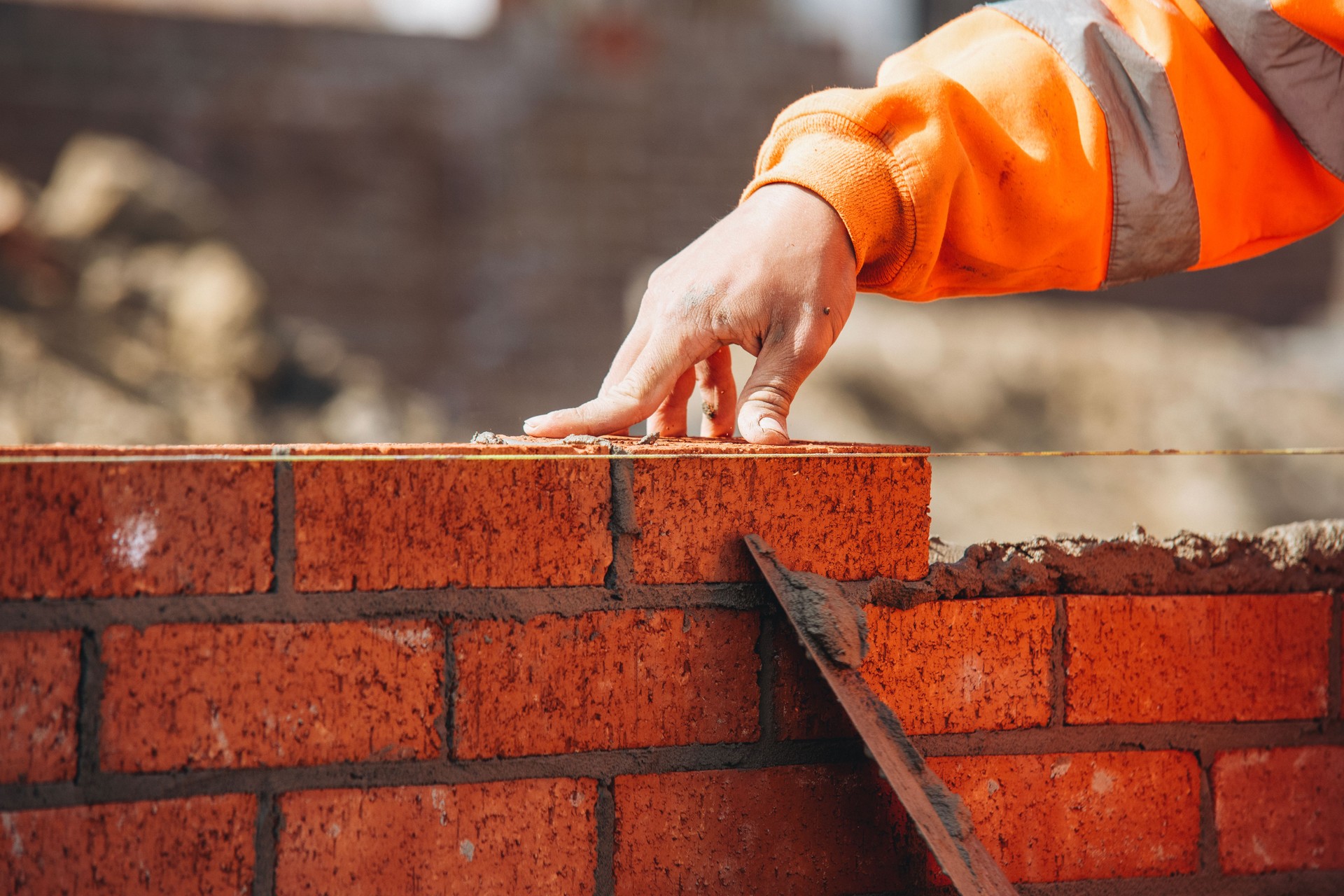 Bricklayer laying another brick in the wall on construction site for sturdy wall