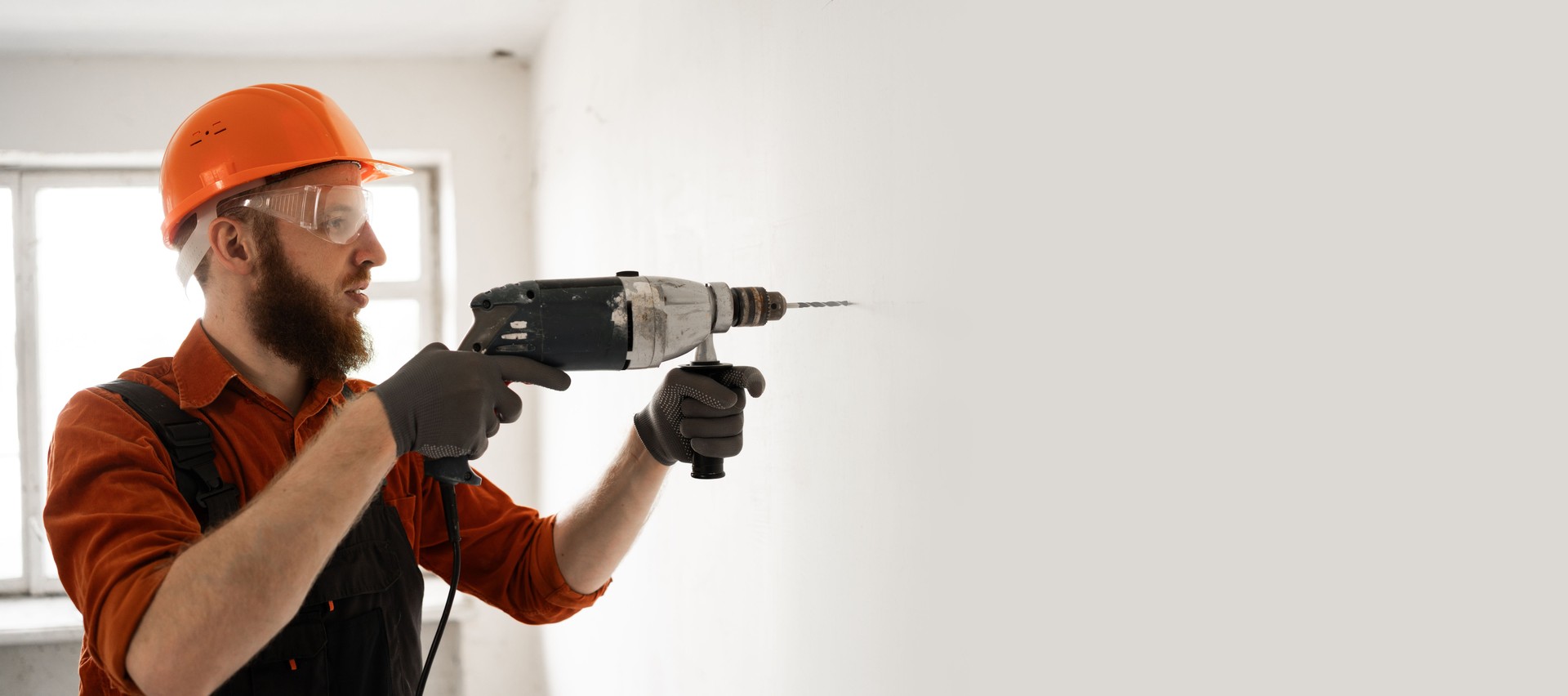 Builder man with a tool using drill on construction site, drilling wall with electric tool
